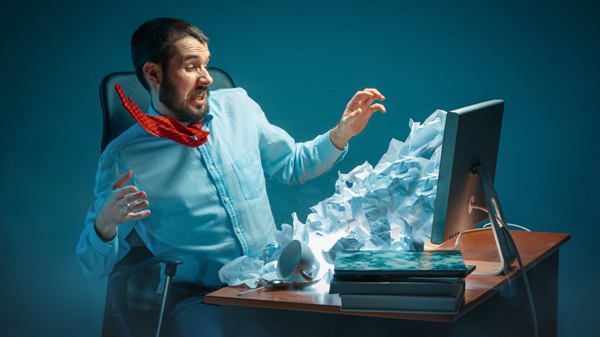 A man shocked by papers pouring out of his computer screen.