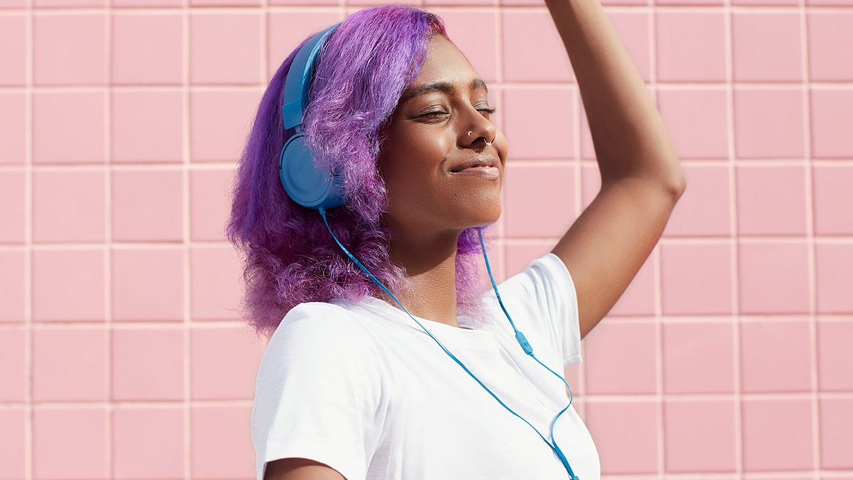 A women wearing blue headphones against a pink tiled wall